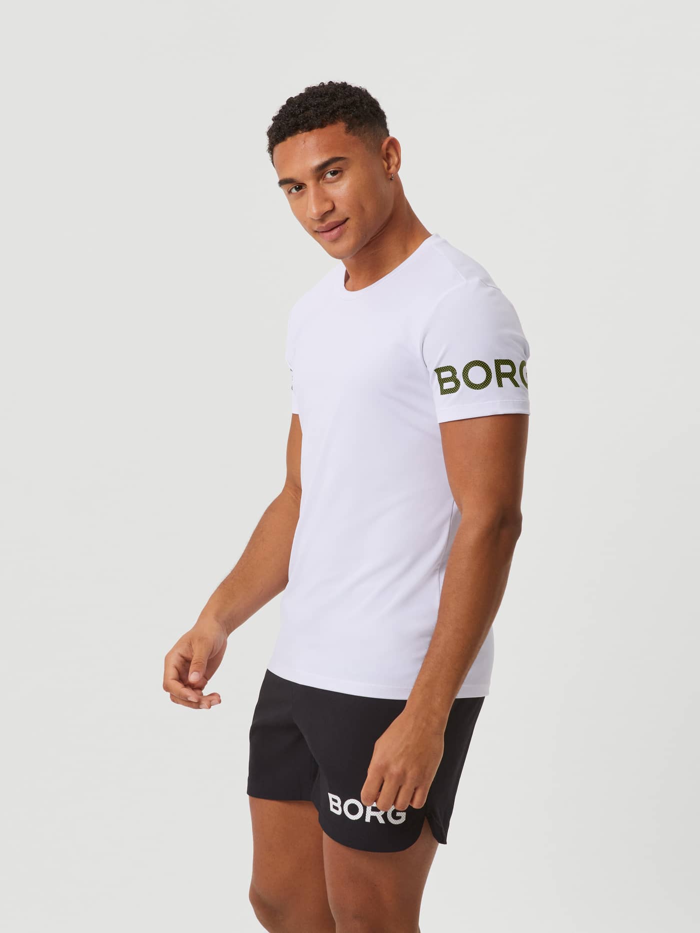 Three-quarter view of a model in the Borg T-Shirt in White Green Logo (White) with a green perforated logo for training. - Image 2