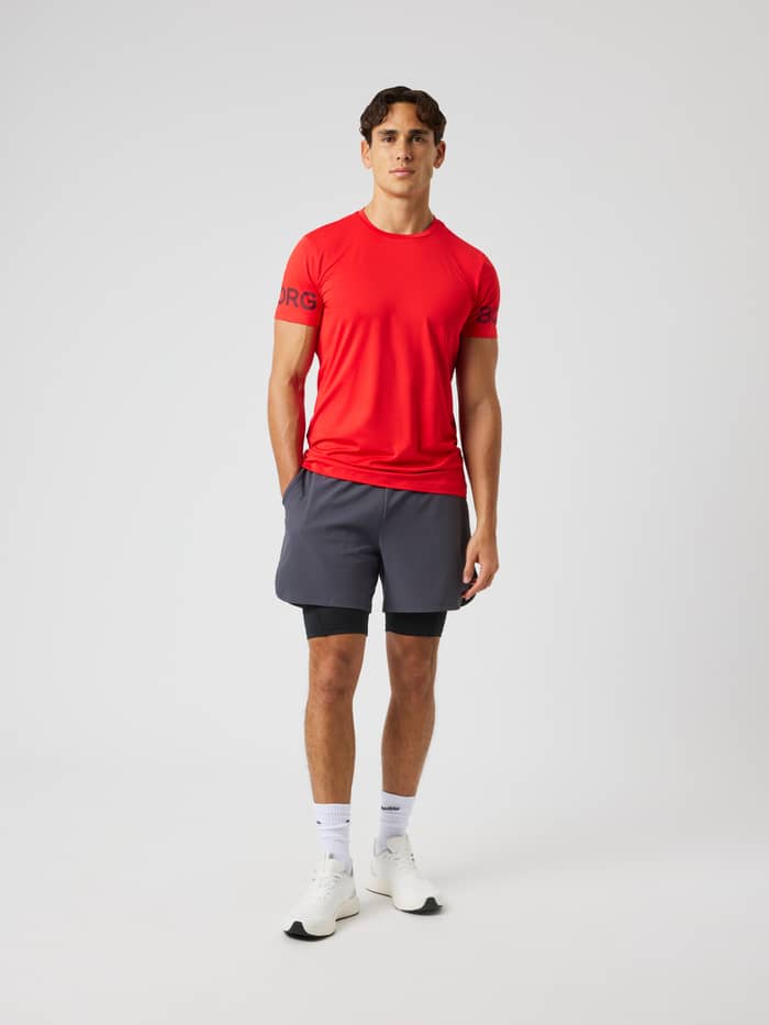 Volledig vooraanzicht van een model in het Borg T-Shirt in Flame Scarlet (Rood) met zwarte mouwlogo's voor training. - Image 4