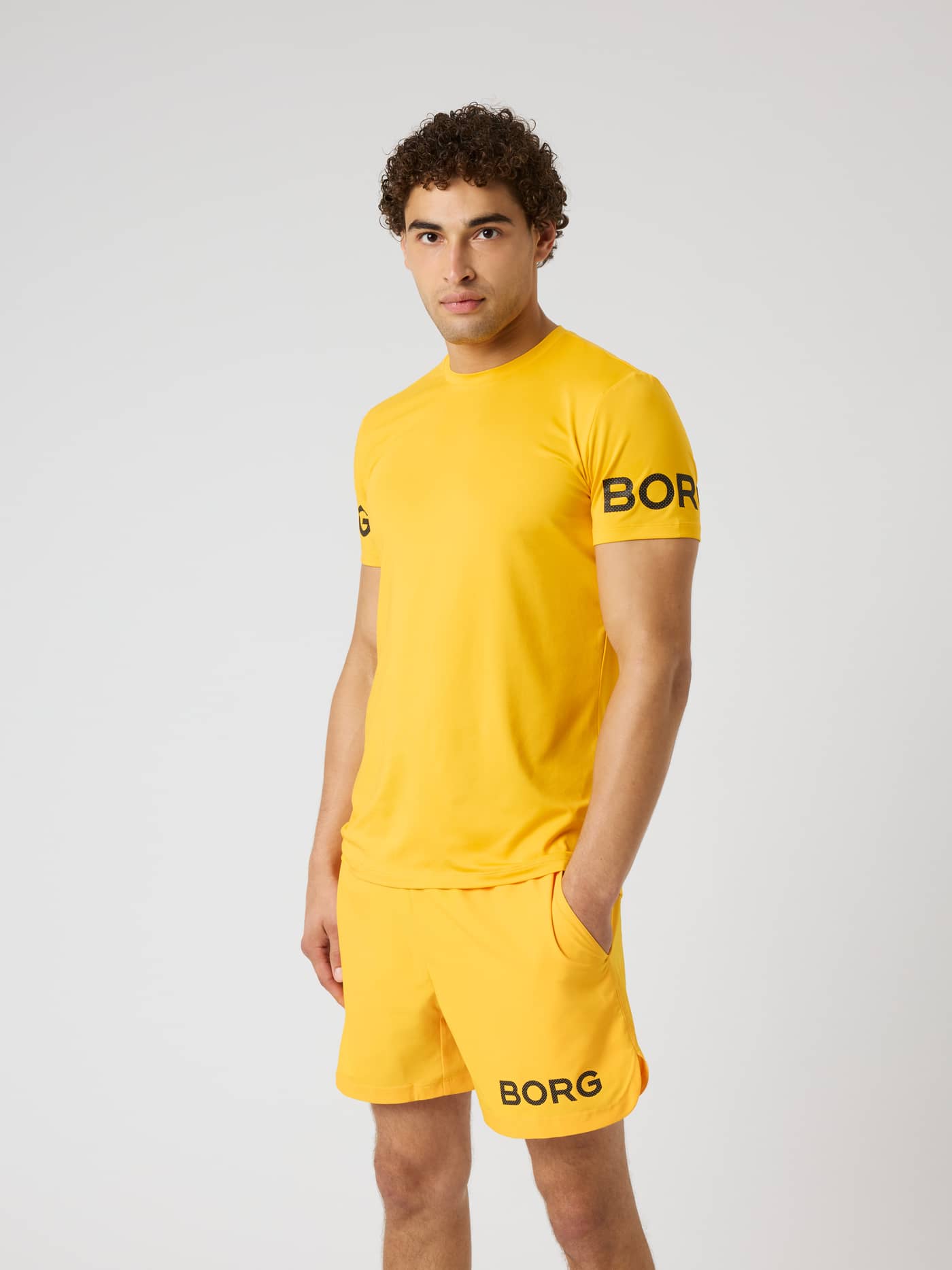 Borg T-shirt i Citrus (Orange) på en mand med sorte ærmelogoer til træning og tennis. - Image 1