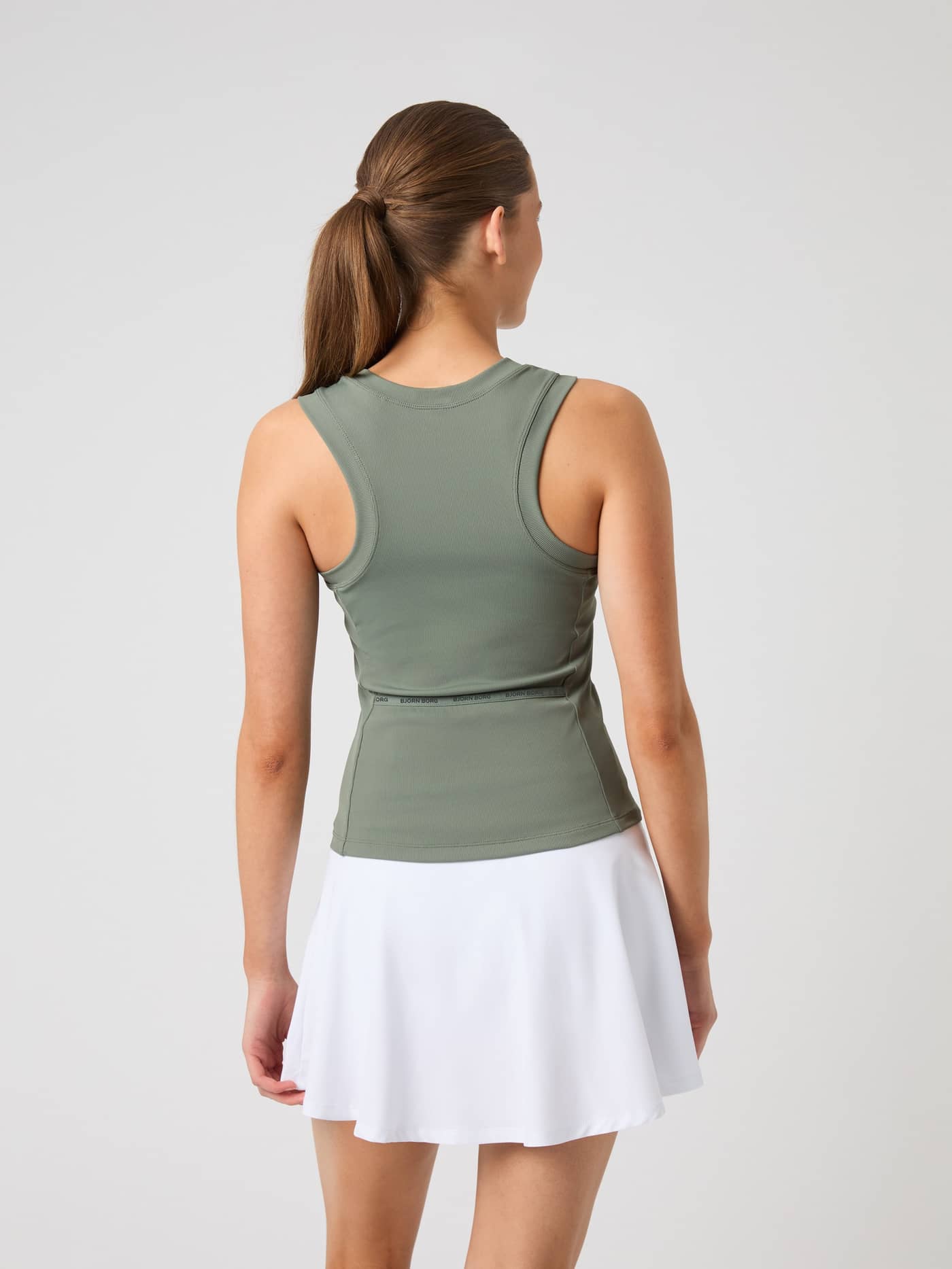 Back view of a model wearing the Björn Borg Ace Pocket Ribbed Tank Top in agave green with a white tennis skirt. - Image 2