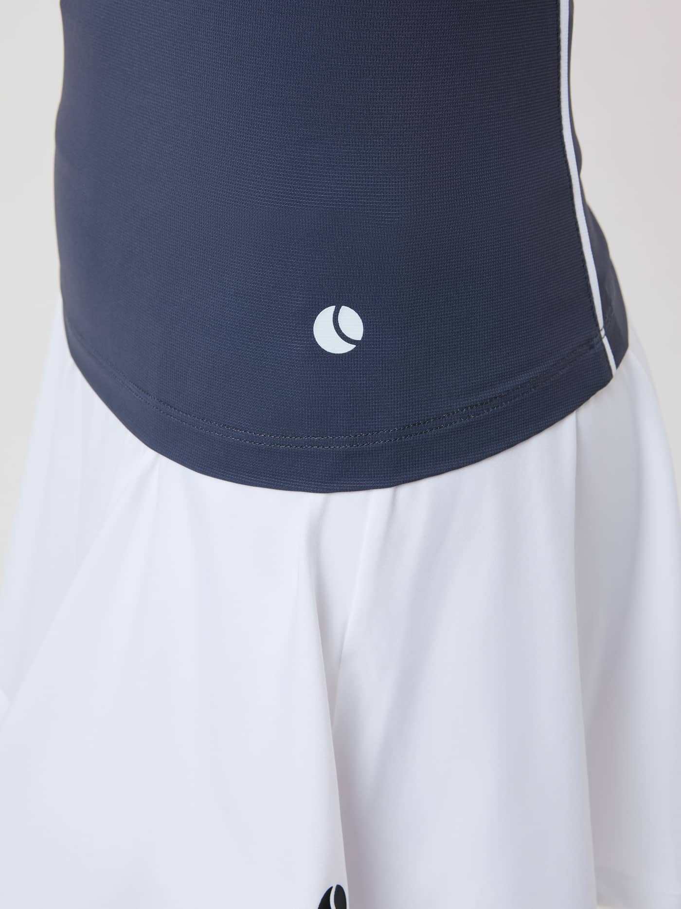 Detailed close-up of the high-stretch Ace V Neck Tank Top in Odyssey Gray (Grey) with a white tennis ball logo on the hip. - Image 5