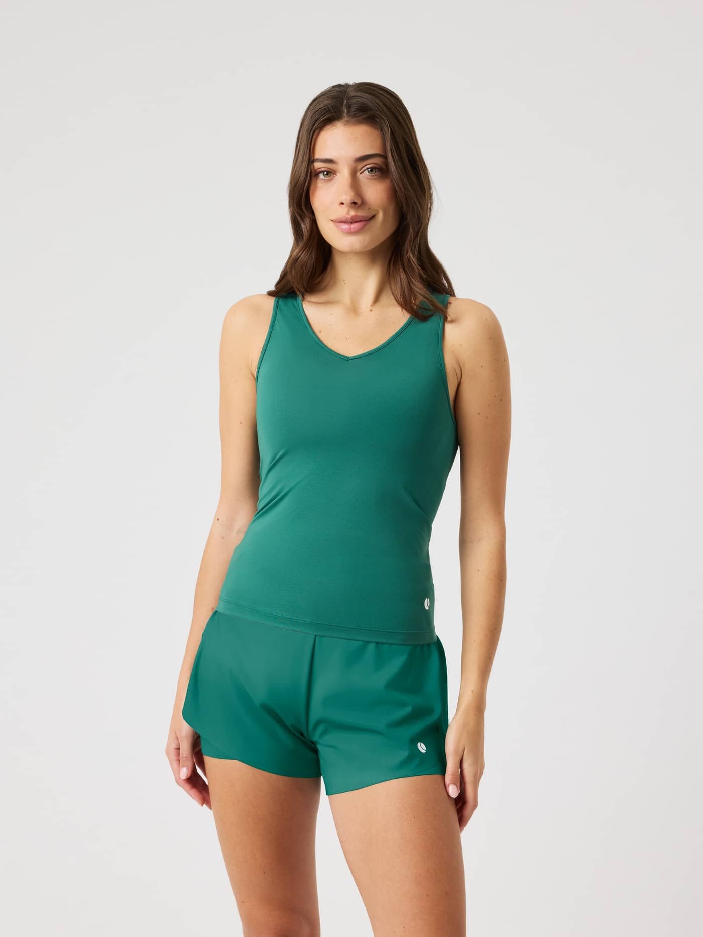 Front view of a model in the slim fit Ace V Neck Tank Top in Posy Green (Green), with a white tennis ball logo on the hip. - Image 1