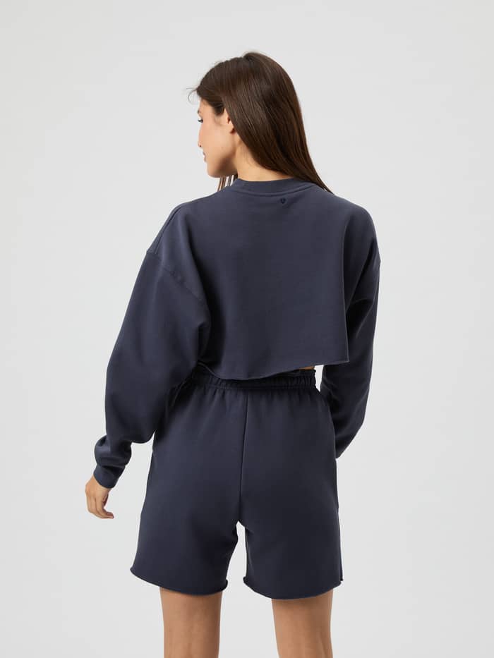 Back view of a woman wearing the Studio Oversized Cropped Sweatshirt in Odyssey Gray (Grey) in a stylish training fit. - Image 3