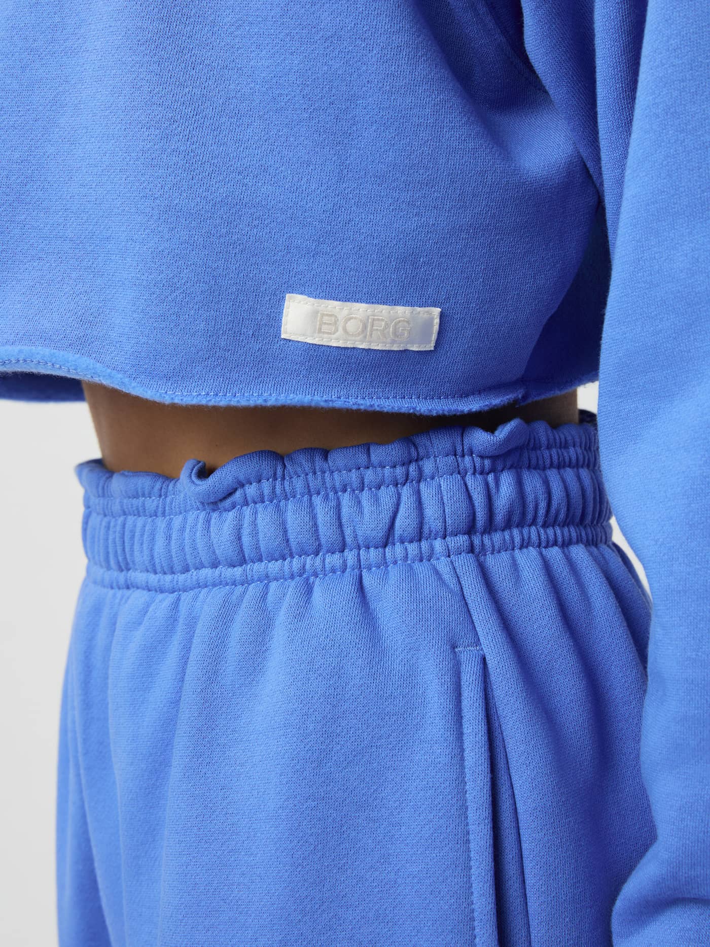 Gros plan du Studio Oversized Cropped Sweatshirt Ultramarine (Bleu) pour femme, bords bruts et étiquette logo Borg blanche. - Image 5