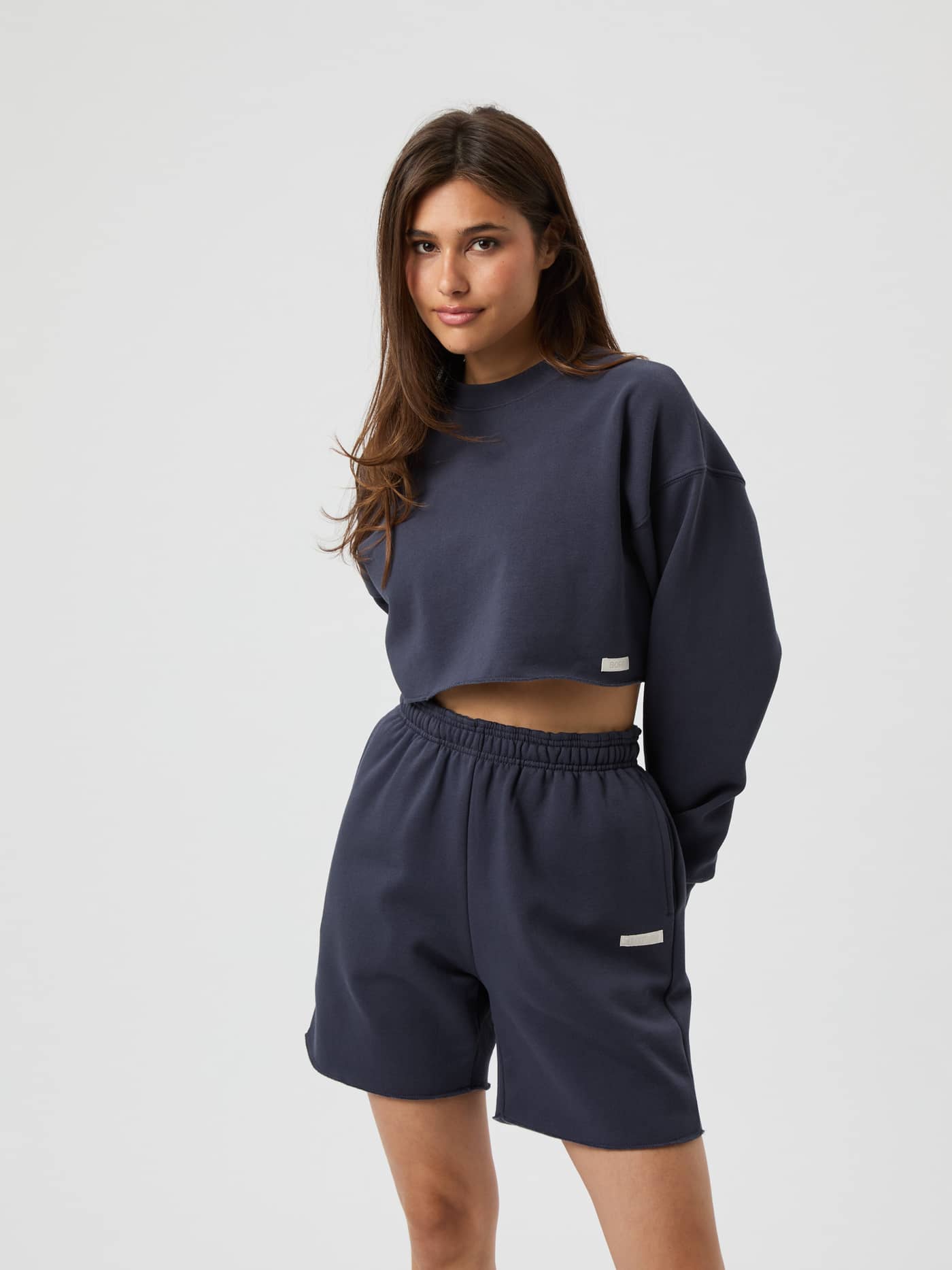 Front view of a woman in the Studio Oversized Cropped Sweatshirt in Odyssey Gray (Grey) with a relaxed fit and white logo. - Image 2