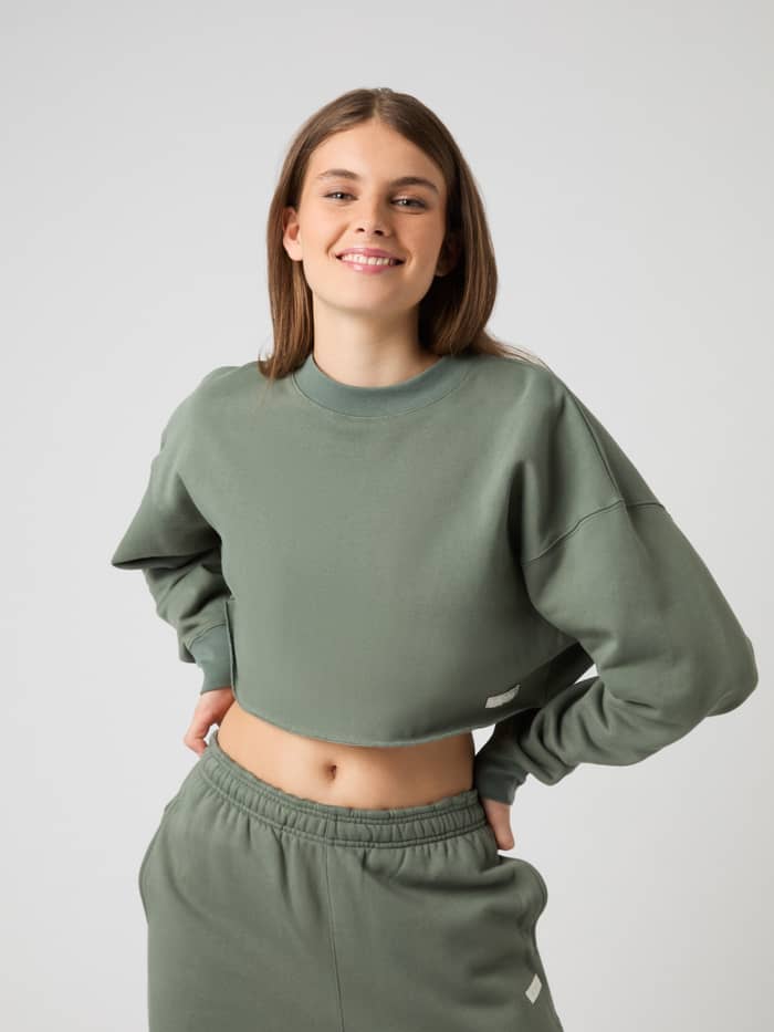 Studio Oversized Cropped Sweatshirt i Agave Green (Grön) i bomull för dam sedd framifrån med vit logoetikett för träning.