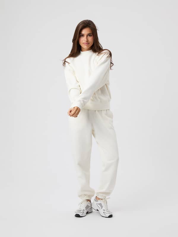 Full-body front view of a woman wearing the Studio Oversized Sweatpants in Cannoli Cream (White) for studio training.