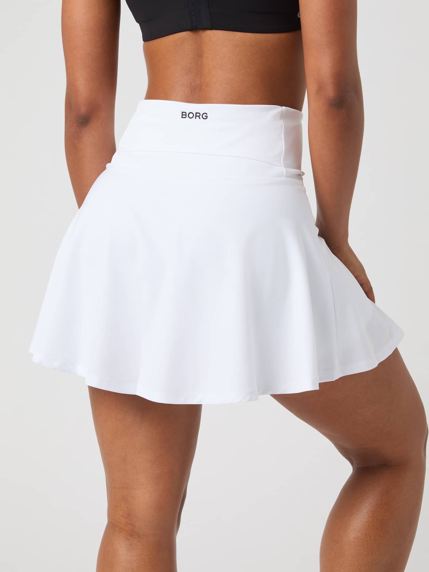 Back view of a model wearing the white Björn Borg Ace Skirt Pocket, showing the logo on the high waistband. - Image 2