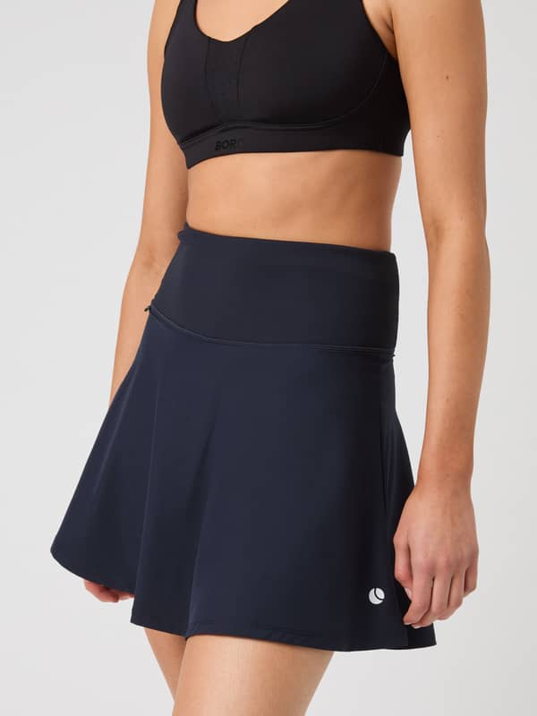 Side view of a model wearing the navy blue Björn Borg Ace Skirt Pocket, showing off its high-waisted and flared fit.