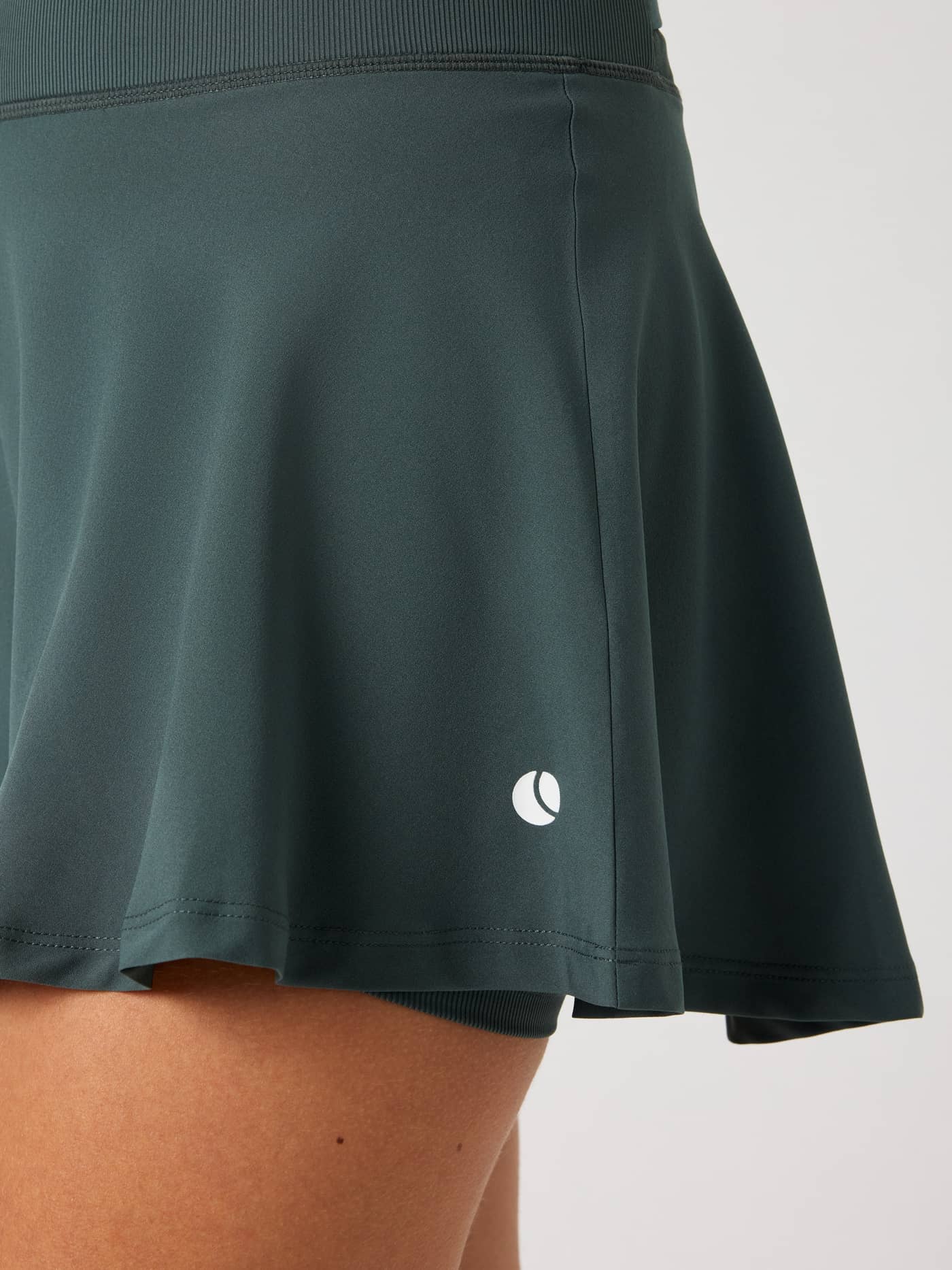 Close-up of the women's Ace Skirt Pocket in Urban Chic (Green) featuring the tennis ball logo and performance fit. - Image 5