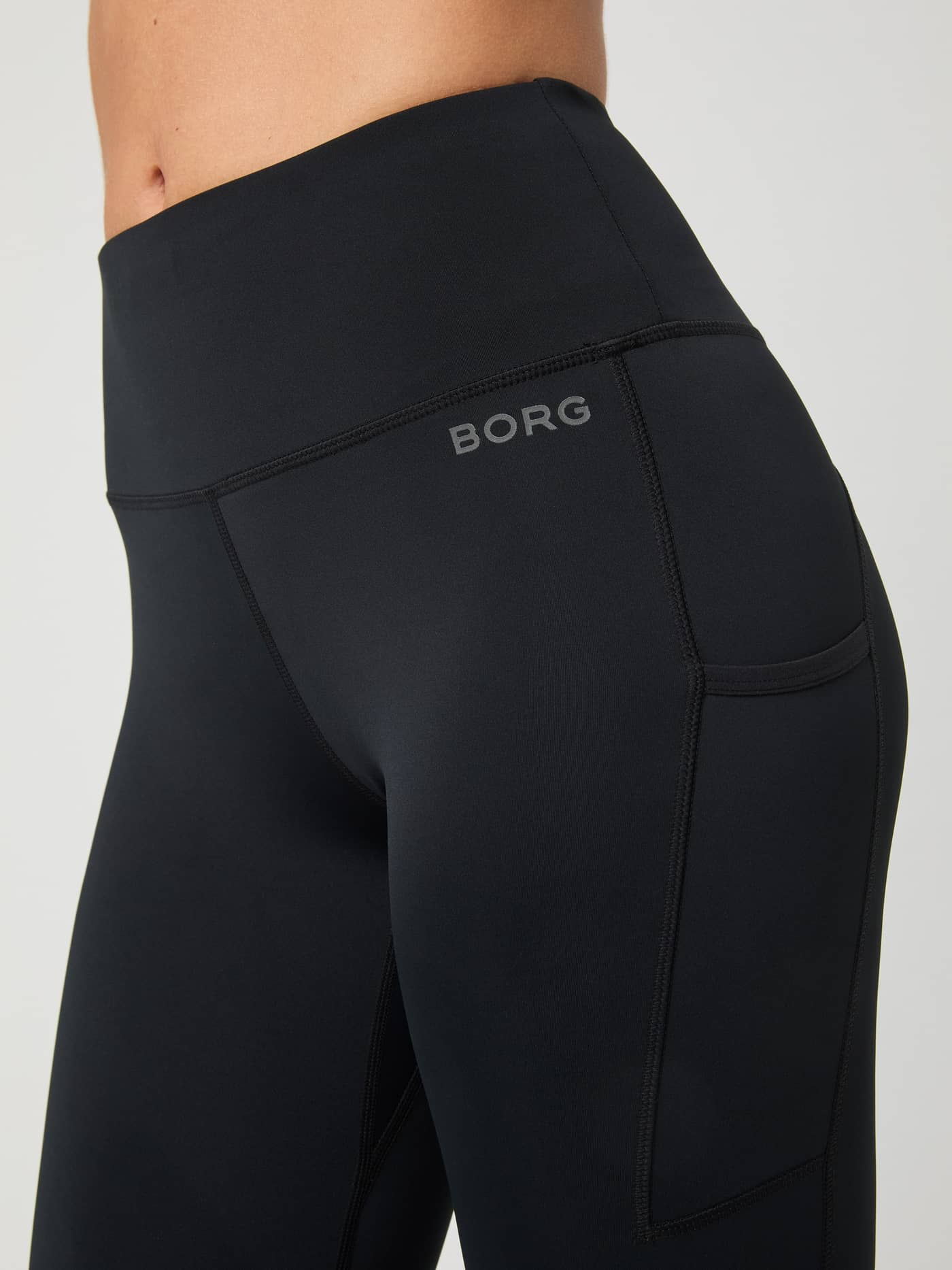 Close-up of the slim fit Borg Running Tights in Black Beauty (Black) featuring a side pocket and grey reflective logo. - Image 6