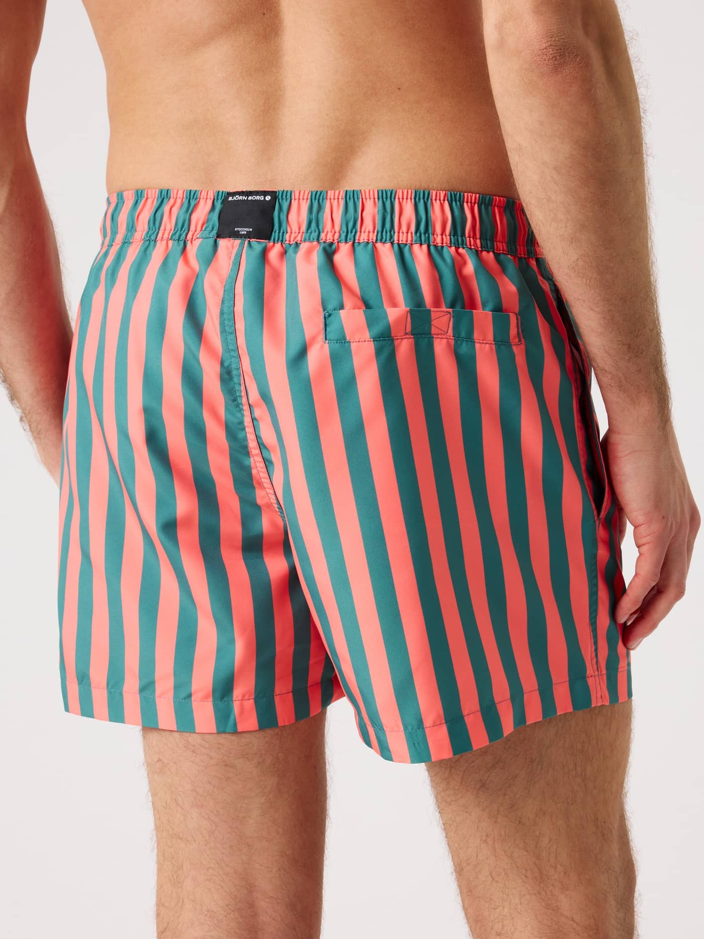 Back view of a man wearing the striped Borg Print Swim Shorts in green and red, crafted from quick-drying recycled polyester. - Image 2