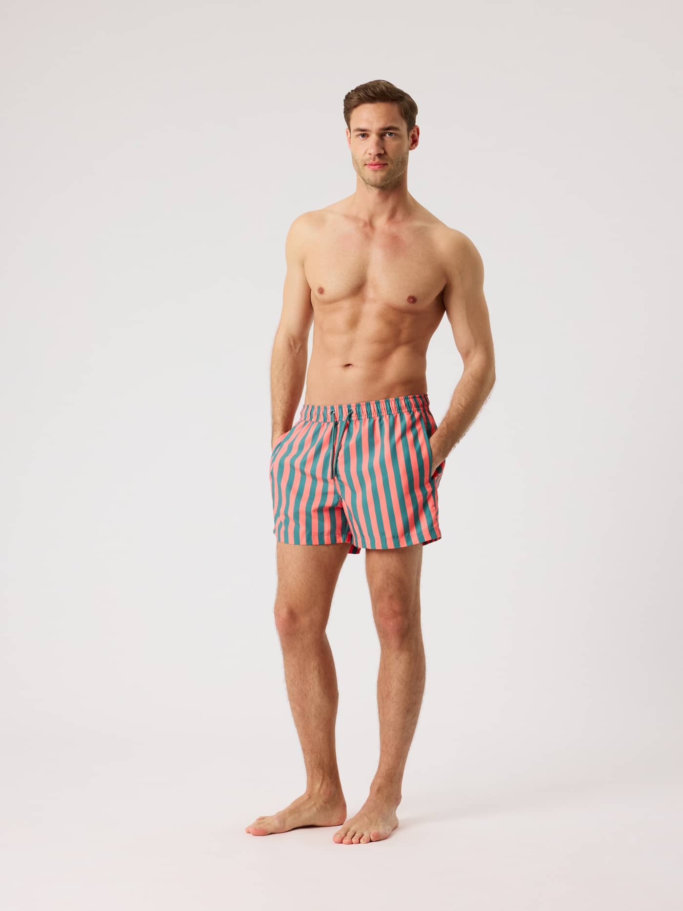 Full-body front view of a man wearing the striped Borg Print Swim Shorts in Parasol 4 (Green, Red) in recycled polyester. - Image 3