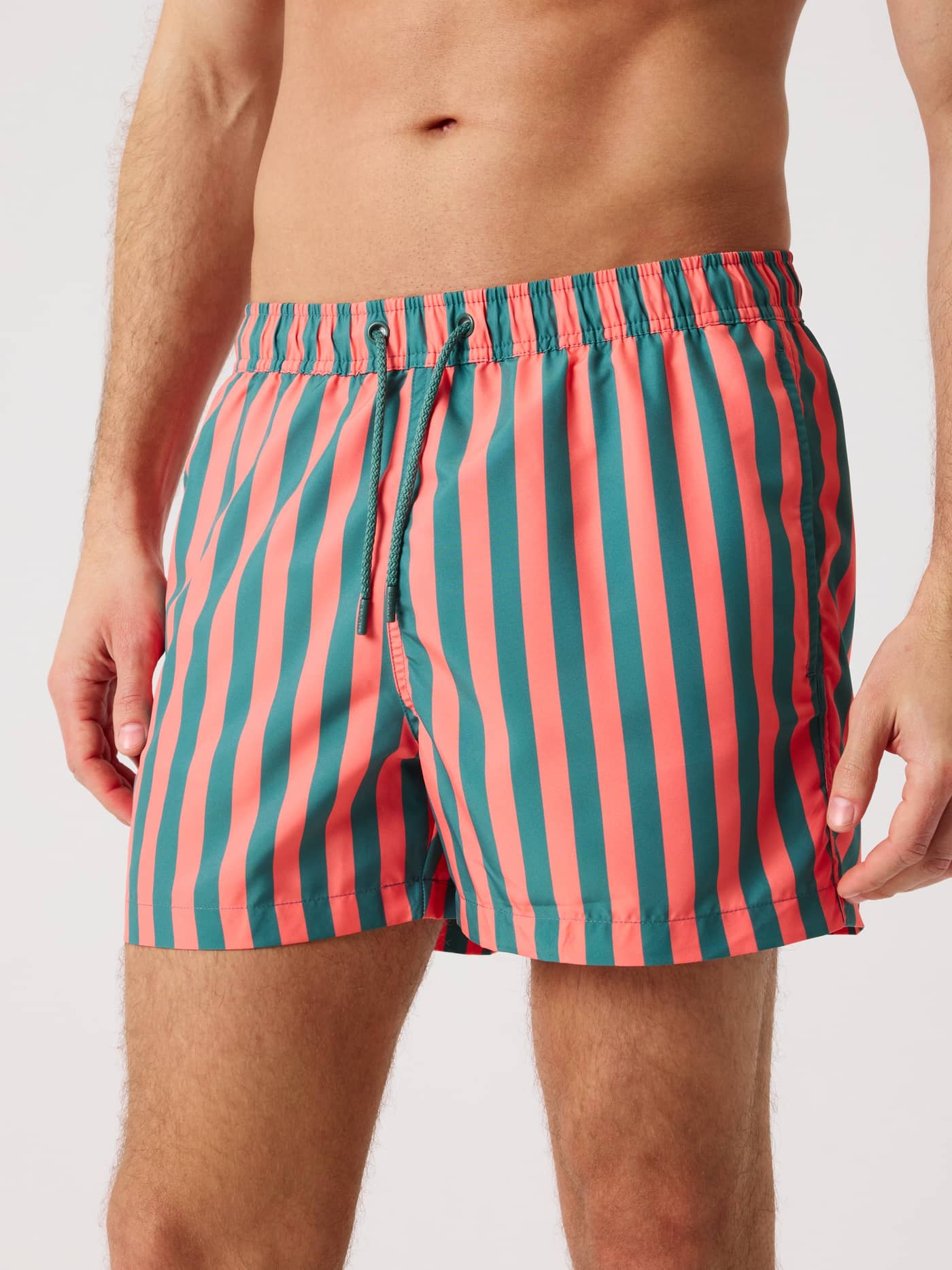 Front view of a man wearing the green and red striped Borg Print Swim Shorts made from quick-drying recycled polyester. - Image 1