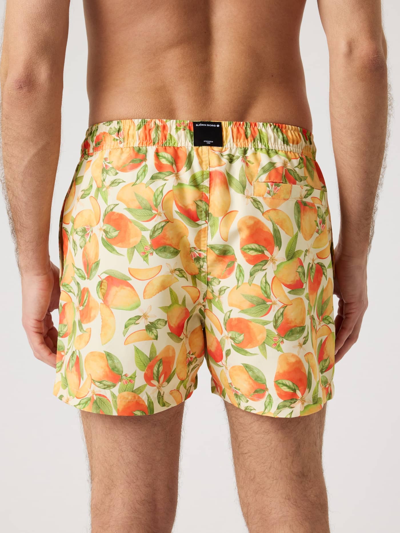 Vista trasera de los Borg Print Swim Shorts en verde, naranja y amarillo con estampado de melocotón y parche de logo negro. - Image 2