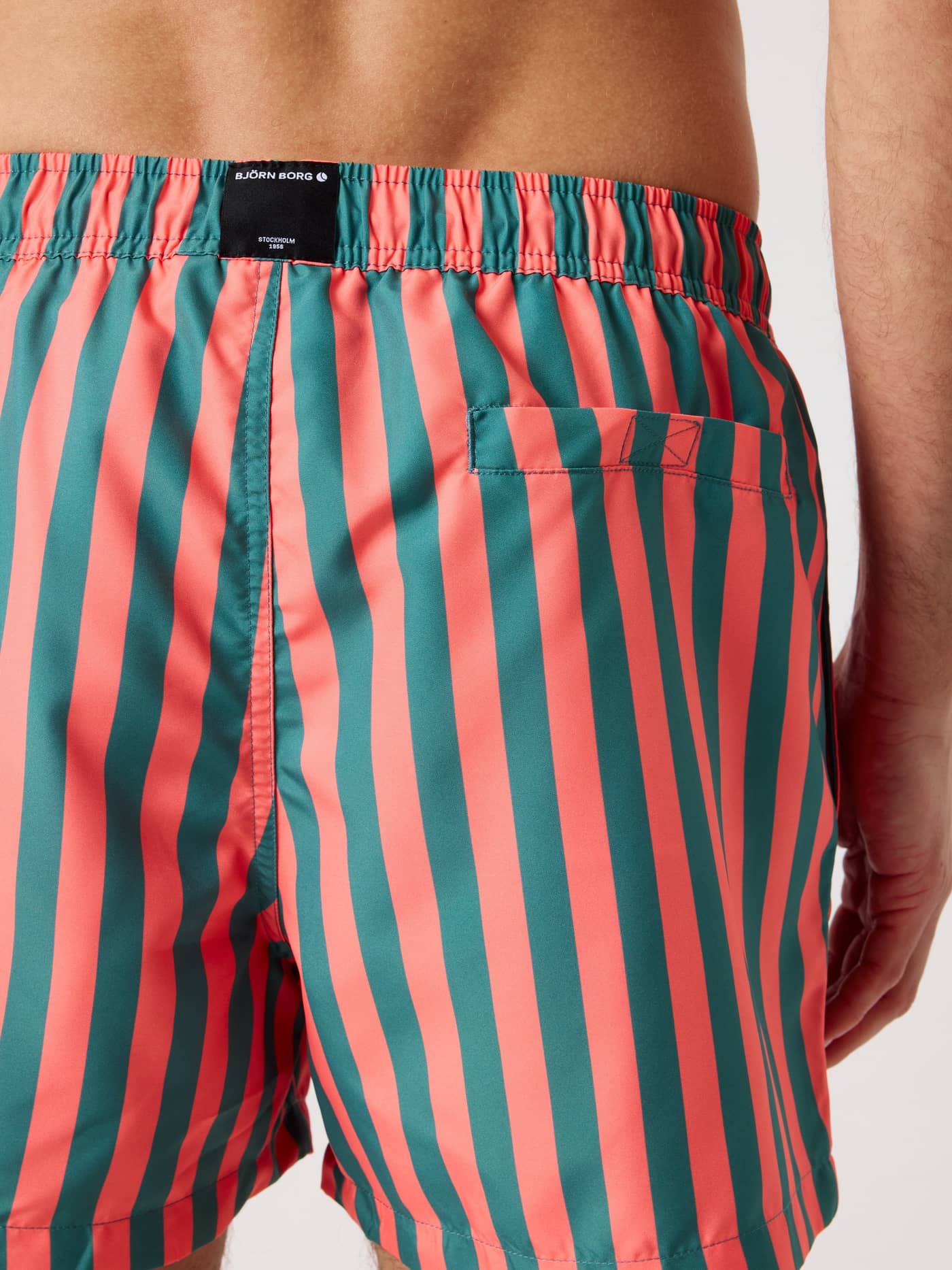 Back view of a man wearing quick-drying striped Björn Borg Print Swim Shorts in Parasol 4 (Green and Red). - Image 4