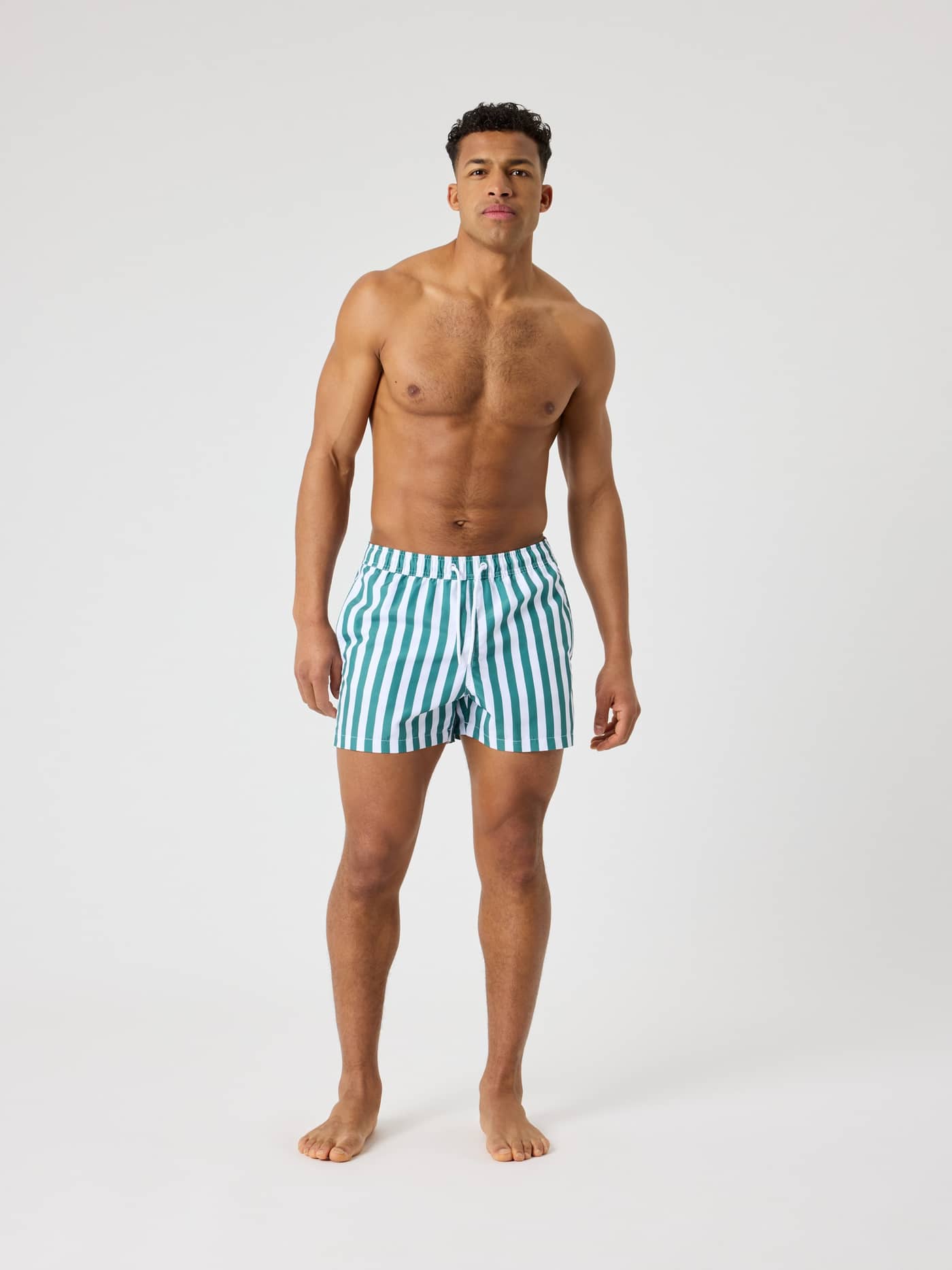 Full-body front view of a man wearing the striped Borg Print Swim Shorts in Parasol 2 (Green and White) with a loose fit. - Image 3
