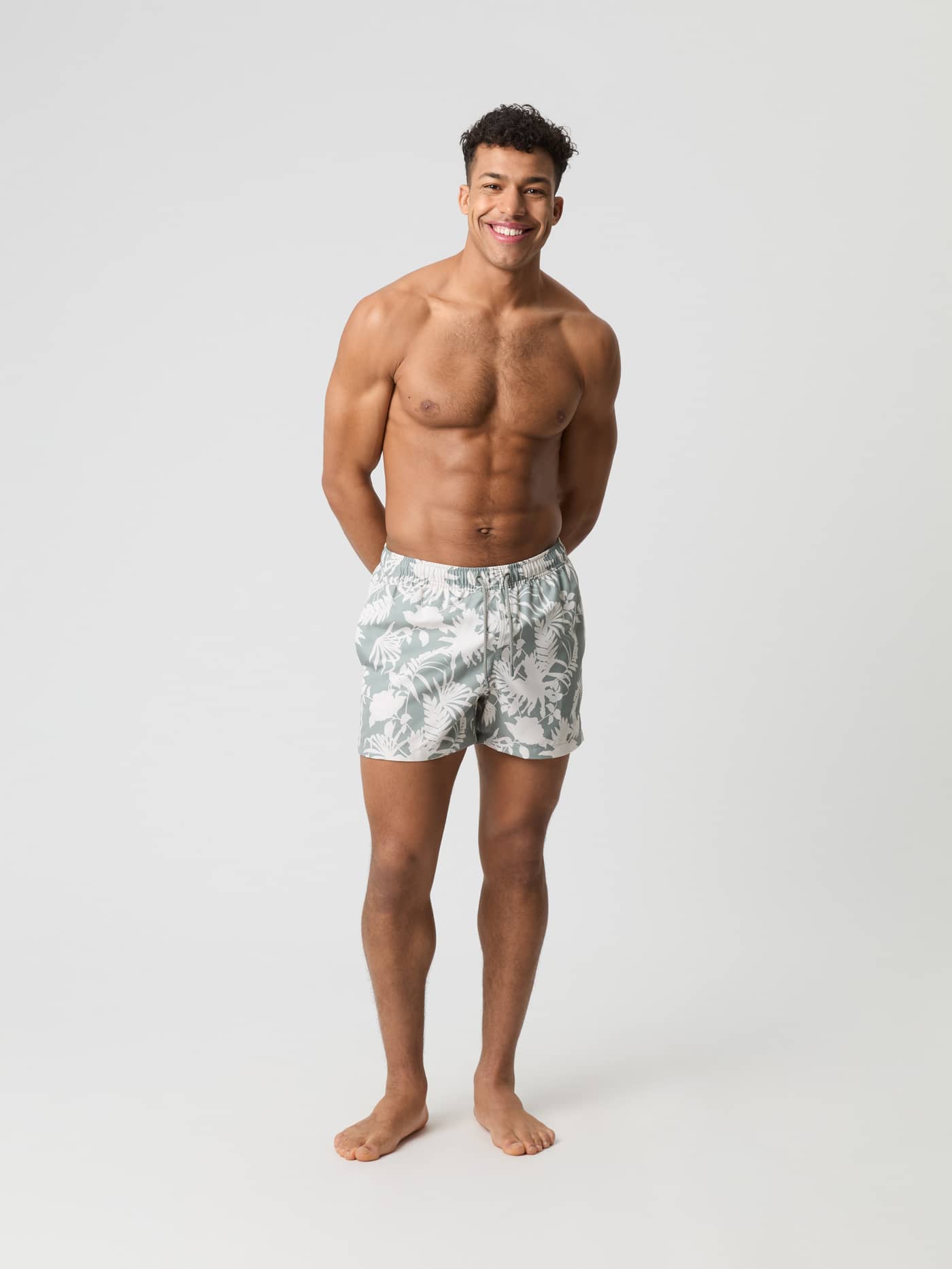 Full-body front view of a man wearing Björn Borg Print Swim Shorts in Dark Jungle 5 (Green) with a leafy pattern. - Image 1