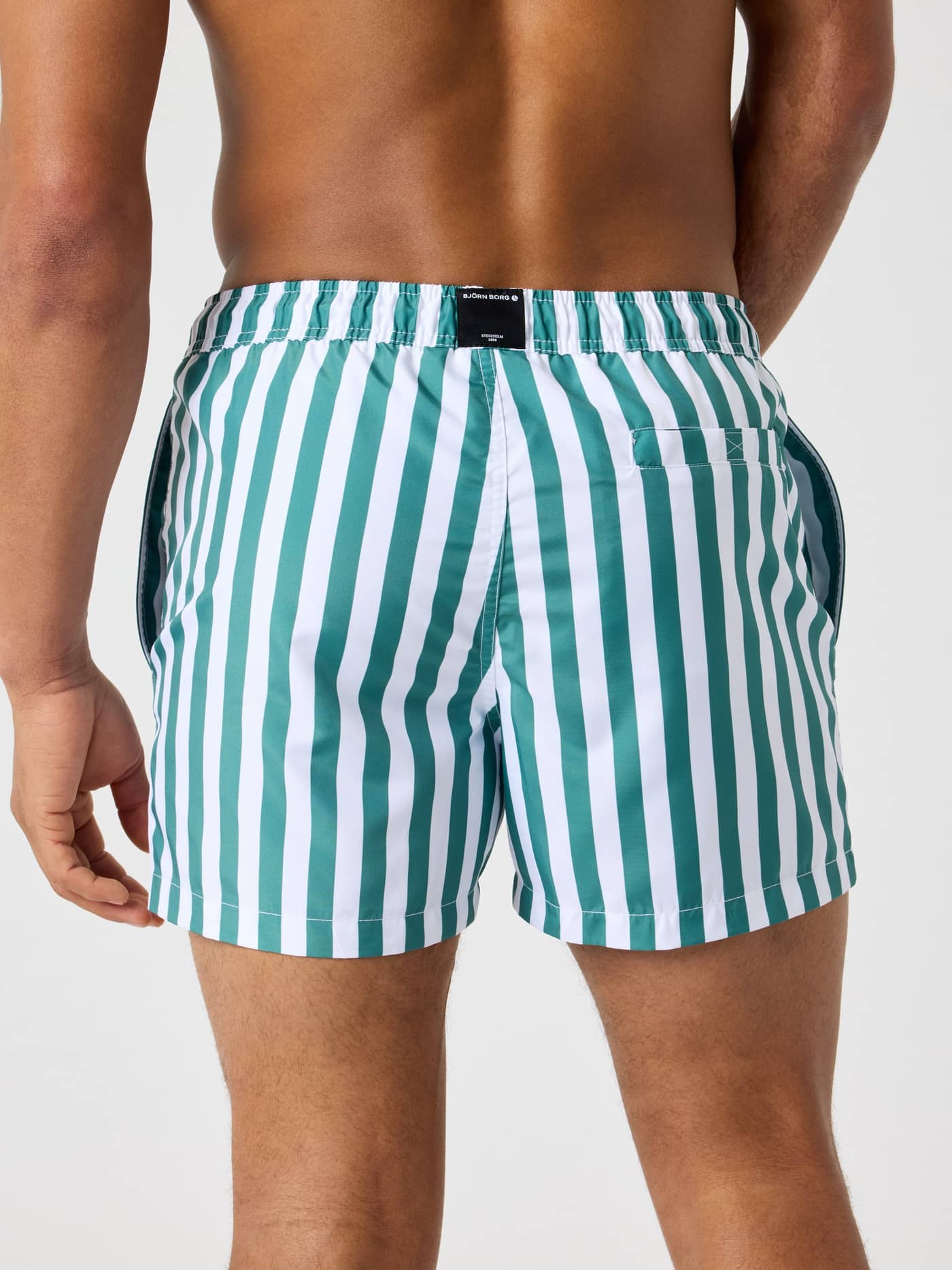 Back view of a man wearing the Borg Print Swim Shorts in Parasol 2 (Green and White) with stripes and a black logo. - Image 2