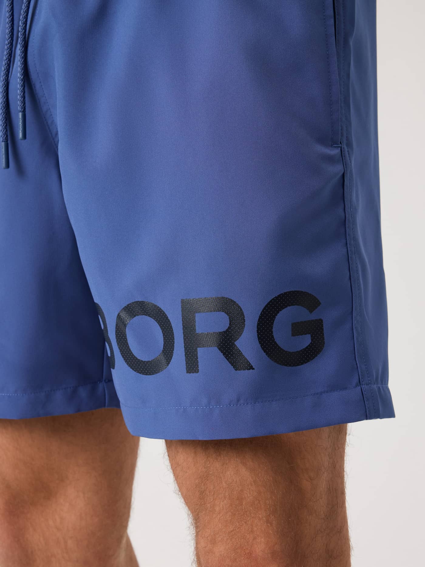 Detalle de los Borg Swim Shorts en Coastal Fjord (Azul) mostrando el logotipo negro en la pernera. - Image 5