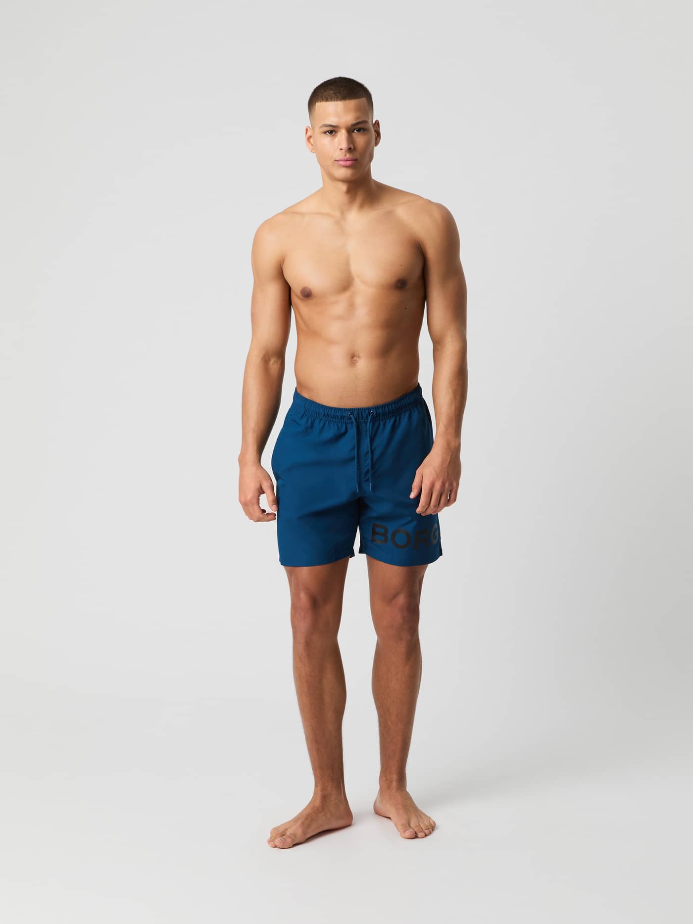 Borg Swim Shorts i Gibraltar Sea (Blå) set forfra på en mand med hurtigtørrende funktion og mørkt logo på benet. - Image 1