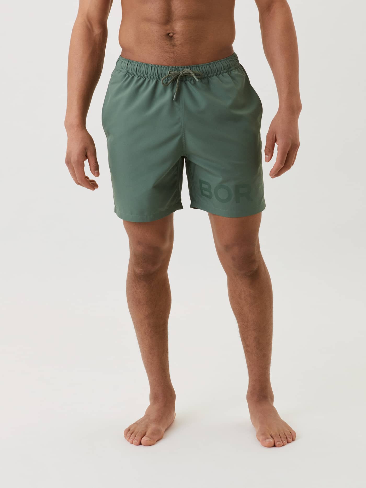 Front view of a man wearing Duck Green (Green) Borg Swim Shorts featuring a tonal logo and an adjustable drawstring. - Image 2