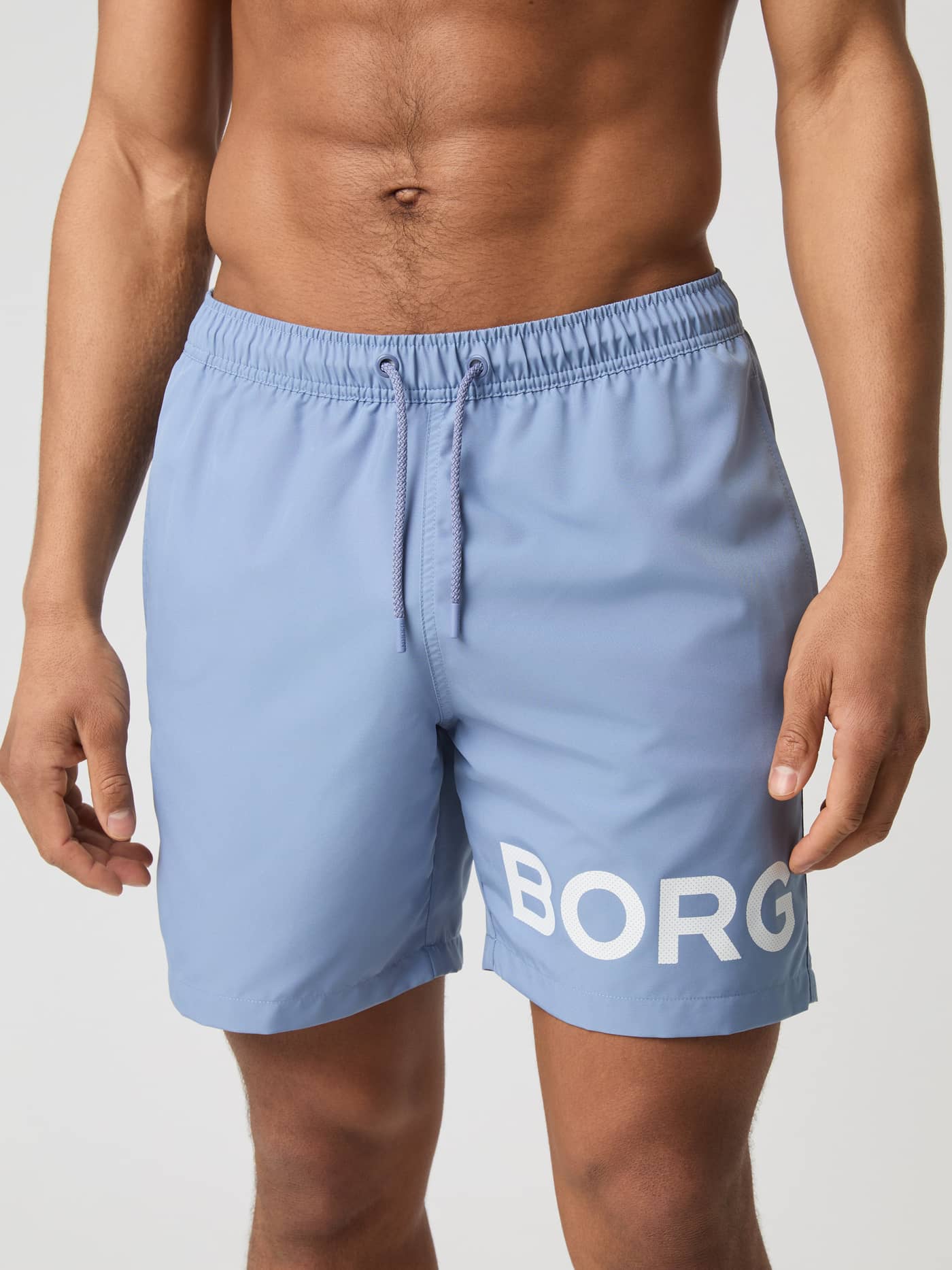Front view of a man wearing the quick-drying Borg Swim Shorts in Stonewash (Blue) with a bold white logo on the leg. - Image 1