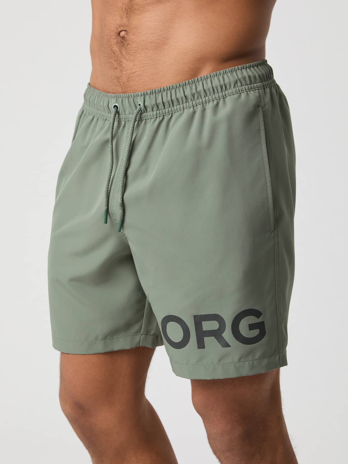 Front view of a man wearing quick-drying Borg Swim Shorts in Agave Green (Green) with a bold black logo. - Image 2