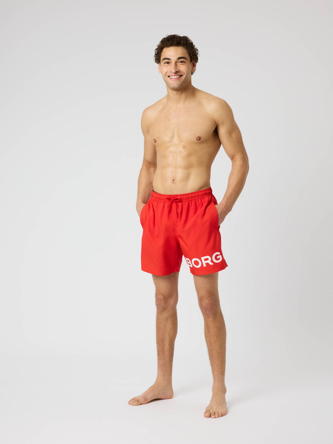Full-body front view of a model wearing Borg Swim Shorts in Flame Scarlet (Red) with a large white logo on the leg. - Image 3