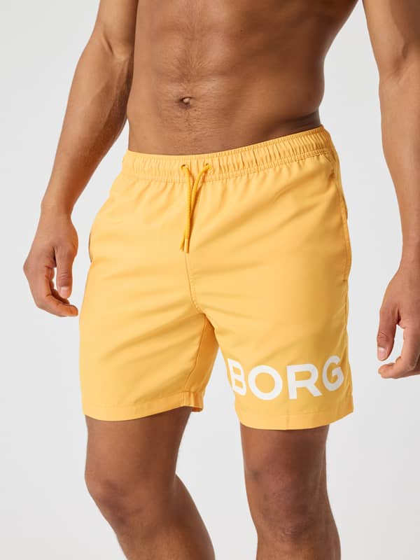 Borg Swim Shorts i Marigold (Gul) med hvidt logo og hurtigtørrende materiale, set forfra på en mand.