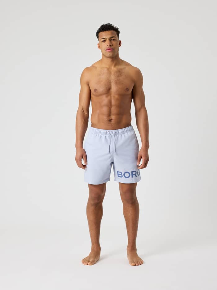 Full-body front view of a man wearing quick-drying Borg Swim Shorts in Icelandic Blue (Blue) with a dark blue logo.