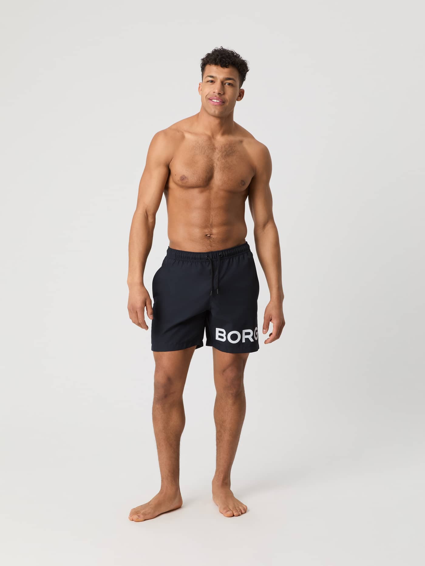 Full-body front view of a man wearing the Borg Swim Shorts in Night sky (Navy) with a bold white logo. - Image 1