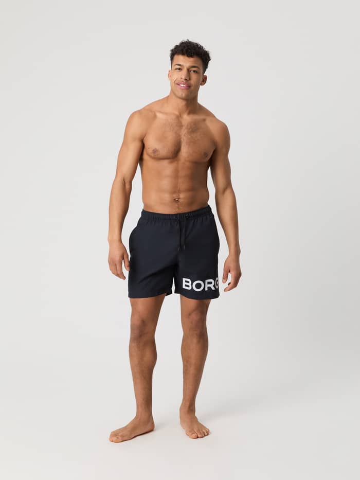 Full-body front view of a man wearing the Borg Swim Shorts in Night sky (Navy) with a bold white logo.