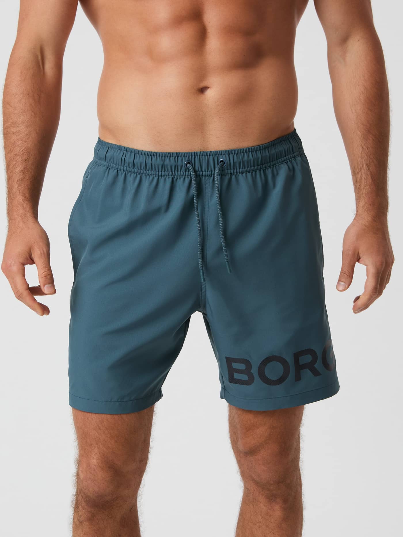Front view of a man wearing the regular fit Borg Swim Shorts in Orion Blue (Blue) with a black logo and drawstring. - Image 2
