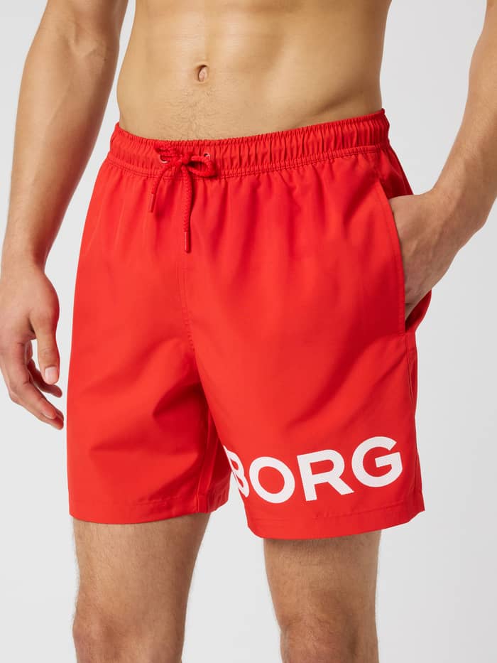 Borg Swim Shorts i Flame Scarlet (Röd) sedda framifrån med ett vitt logotryck på benet för herrar.