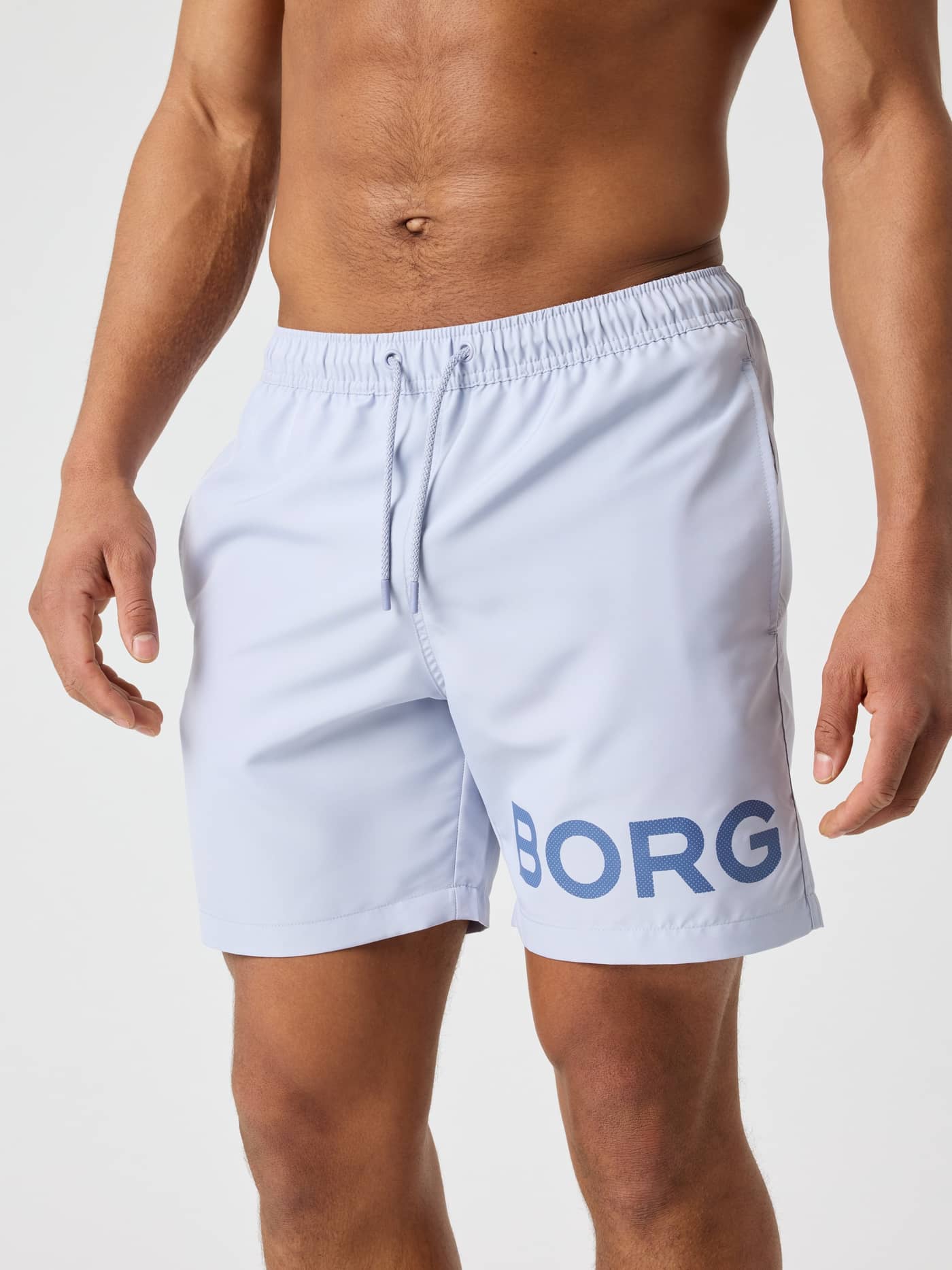 Front view of a man wearing Icelandic Blue (Blue) Borg Swim Shorts, featuring a drawstring waist and dark blue logo. - Image 1