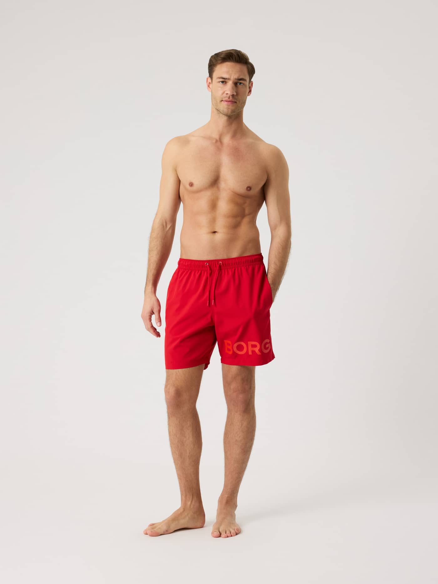 Full-body front view of a man wearing quick-drying, regular fit Borg Swim Shorts in Pompeian Red (Red) with a large leg logo. - Image 3