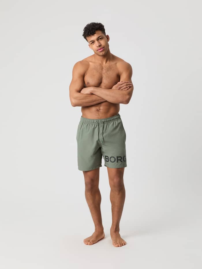 Mann i fullfigur forfra iført hurtigtørkende Borg Swim Shorts i Agave Green (Grønn) med sidelommer og svart logo.