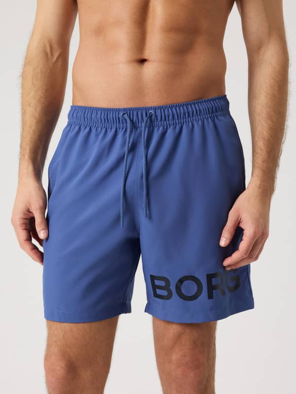 Front view of a man wearing the regular fit Björn Borg Swim Shorts in Coastal Fjord (Blue) with a black logo.