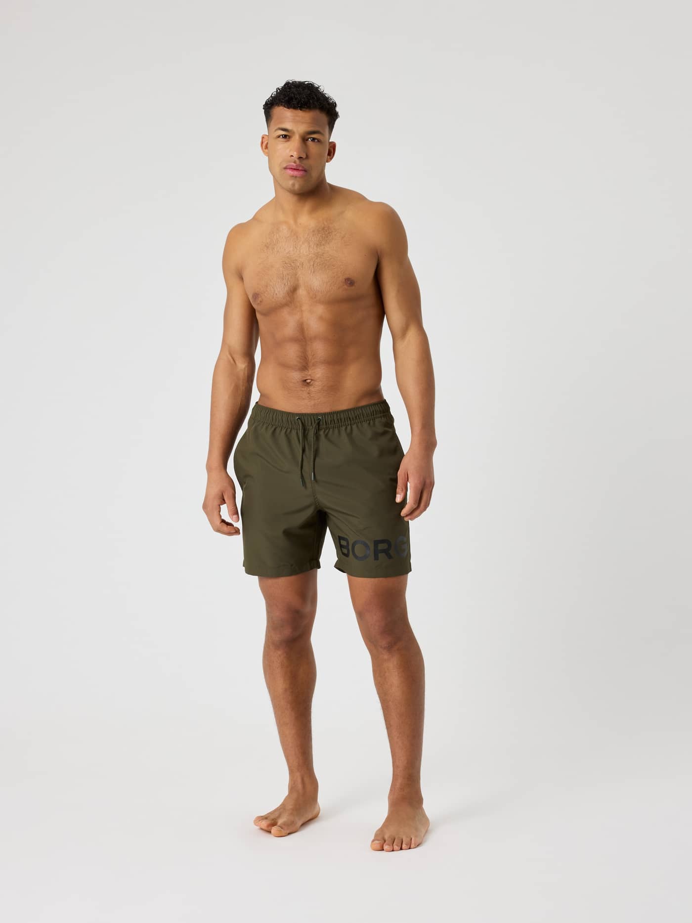 Front view of a man wearing the Borg Swim Shorts in Forest Night (Green) featuring a bold logo on the leg. - Image 3