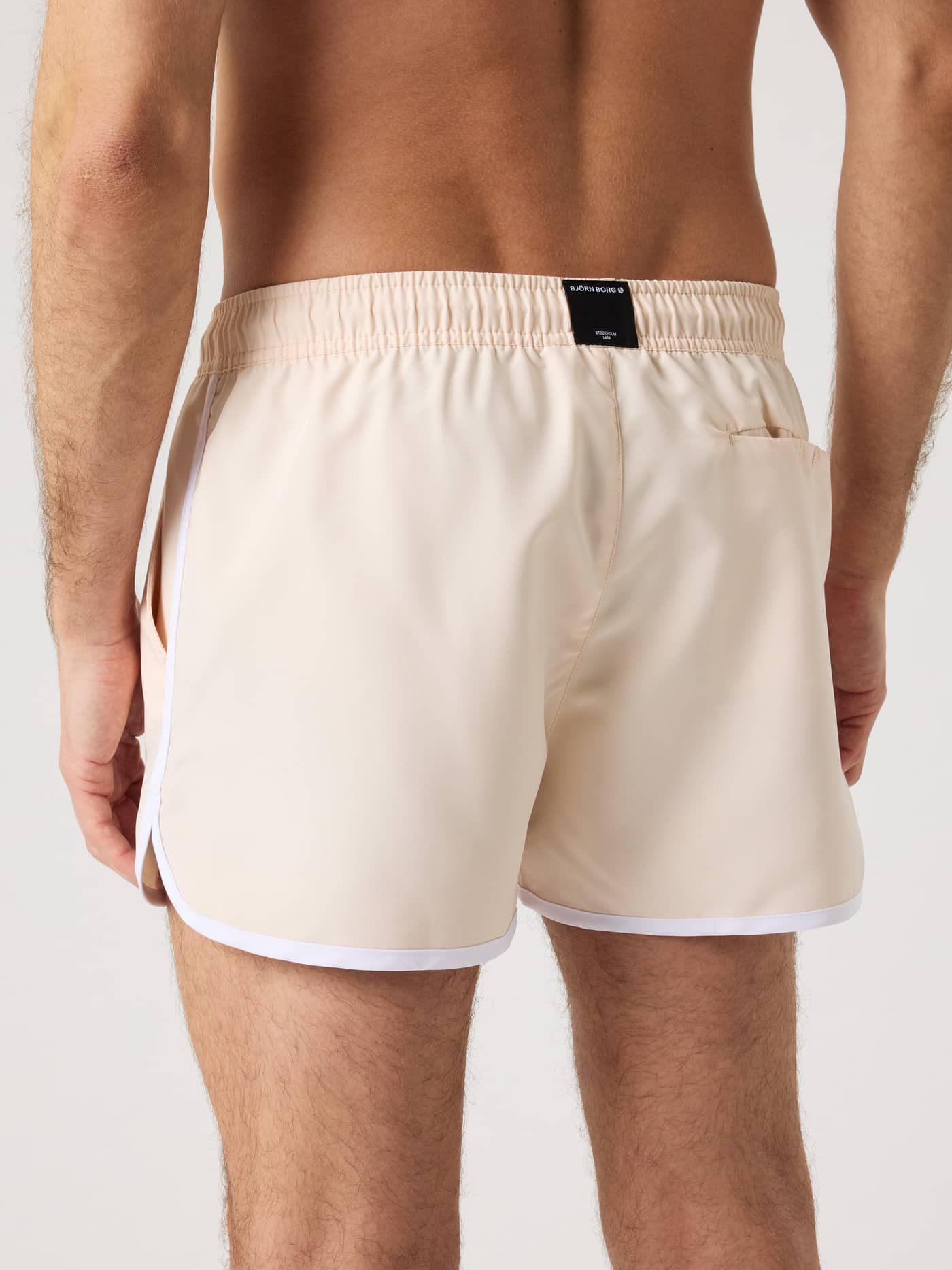 Back view of a man wearing the Borg Retro Swim Shorts in Creme De Peche (pink) with white trim and a black logo. - Image 2