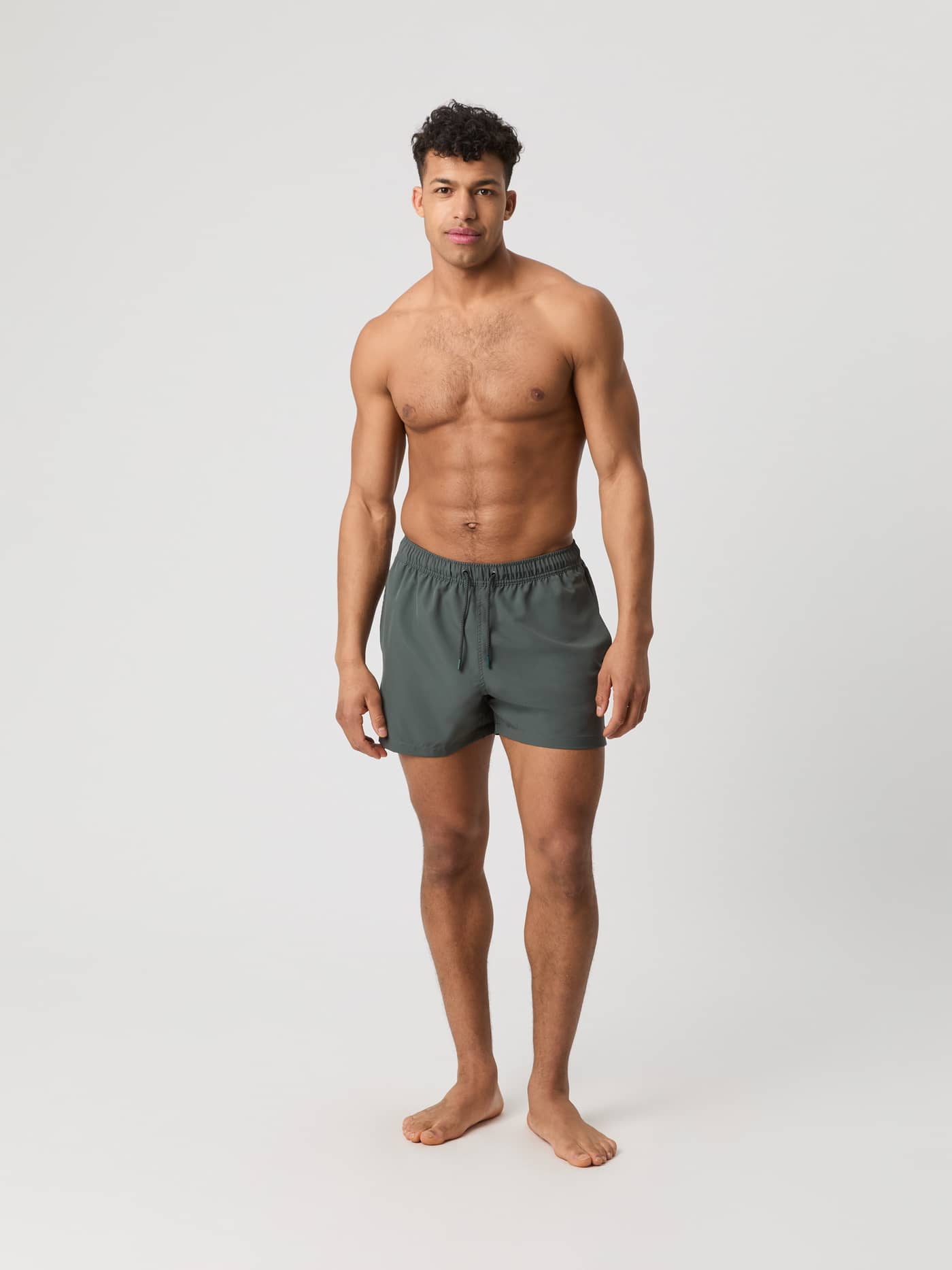 Full-body front view of a man wearing the Borg Solid Swim Shorts in Urban Chic (Green), featuring a loose fit. - Image 1