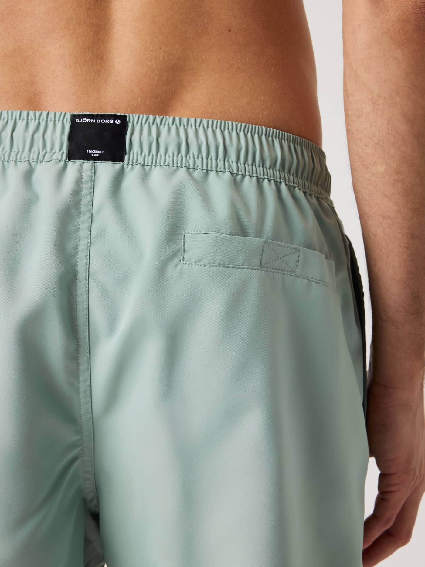 Back view of a man wearing the Borg Solid Swim Shorts in Green featuring a Velcro pocket and black woven logo label. - Image 4