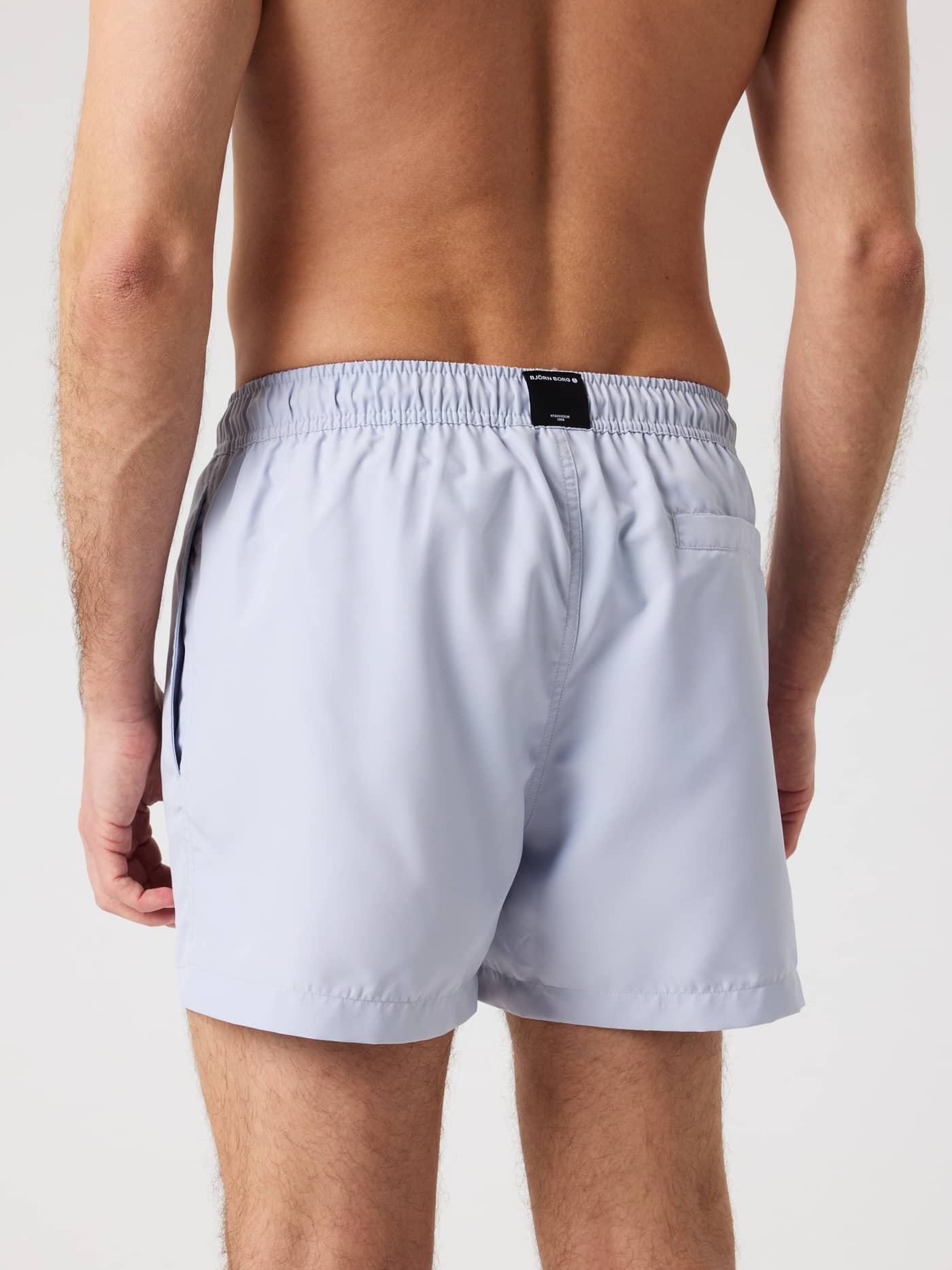 Back view of a man wearing the Björn Borg Solid Swim Shorts in Icelandic Blue (Blue) with a loose fit and a black logo label. - Image 2