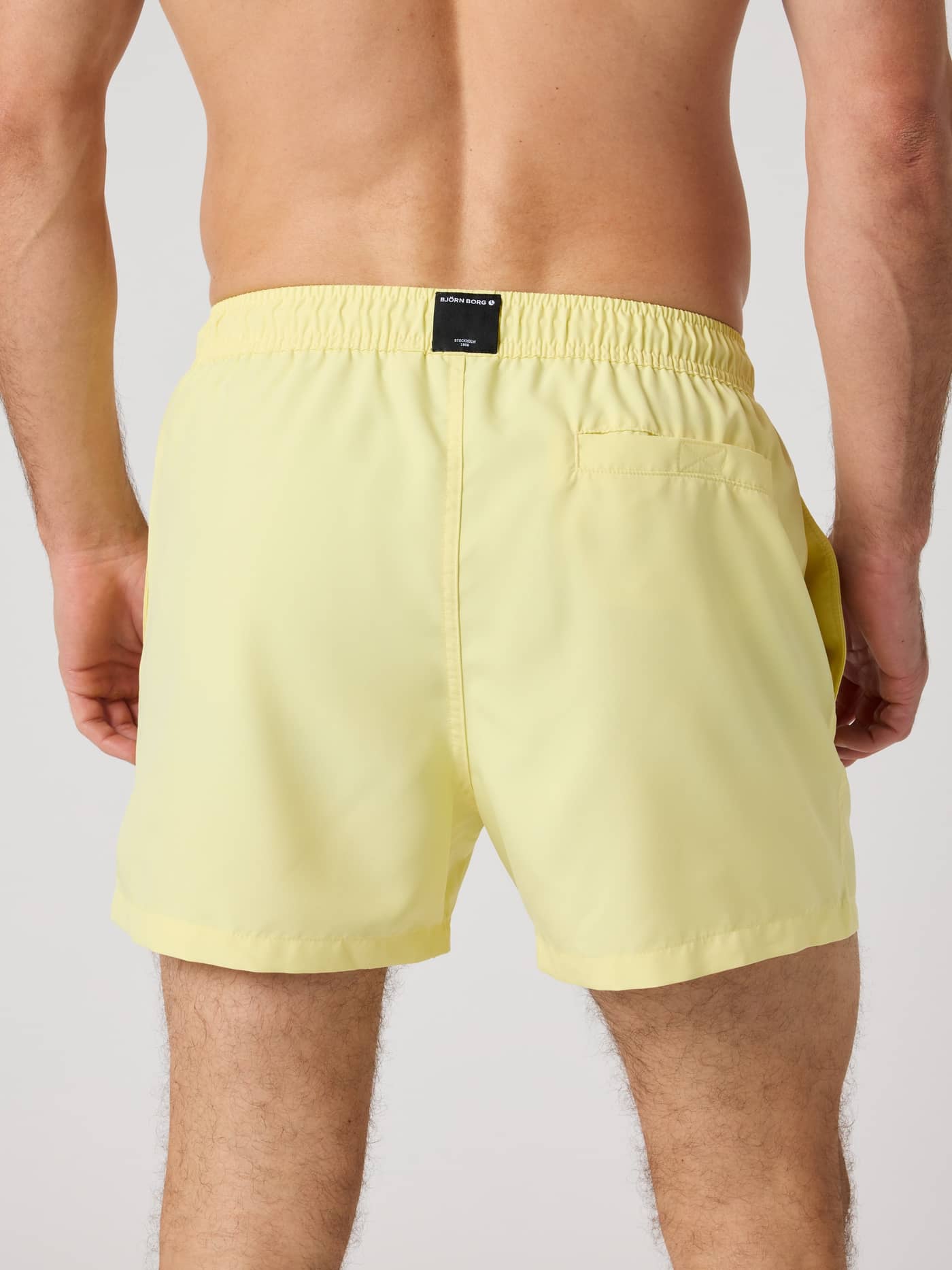 Back view of a man wearing the Borg Solid Swim Shorts in Lemonade (Yellow), highlighting the functional back pocket. - Image 2