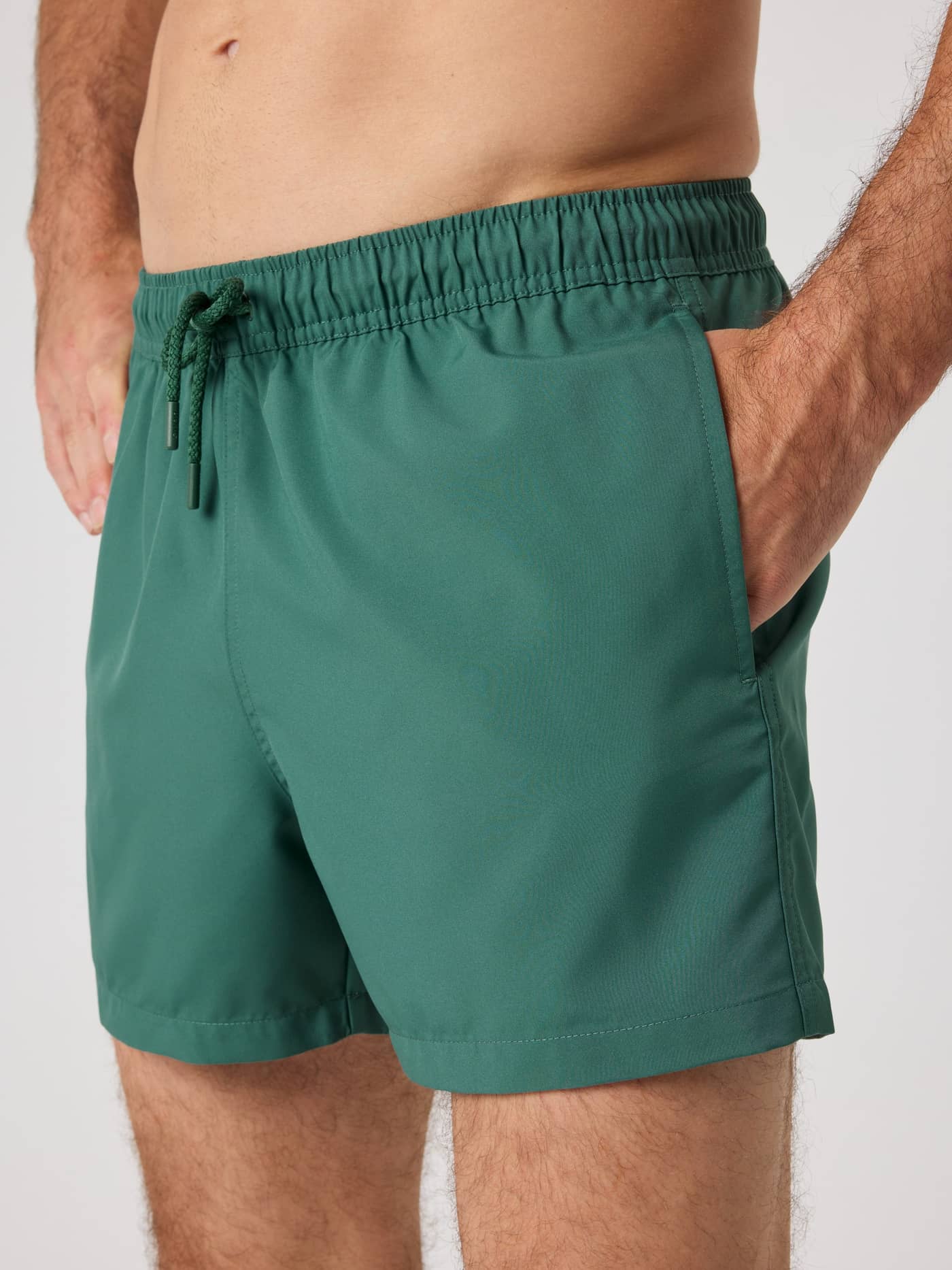 Side view of a man wearing the loose fit Borg Solid Swim Shorts in Mallard Green (Green), showing the side pocket. - Image 4