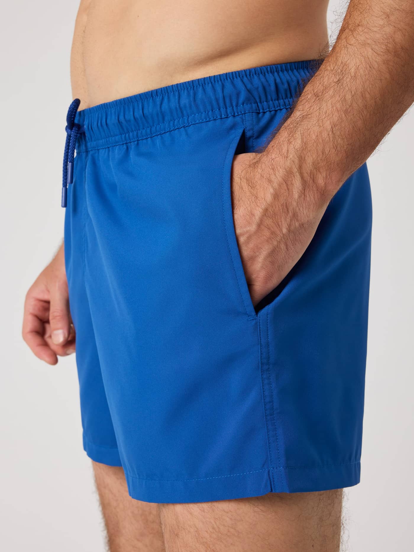 Side view of a man wearing the loose-fitting Björn Borg Solid Swim Shorts in Monaco Blue (Blue) with side pockets. - Image 4