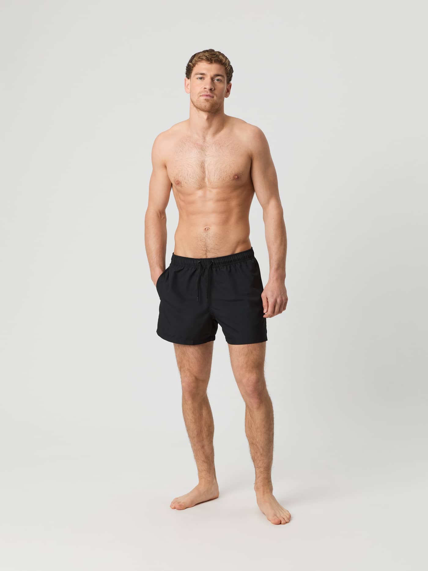 Full-body front view of a man wearing loose Borg Solid Swim Shorts in Black Beauty (Black) made from recycled polyester. - Image 2