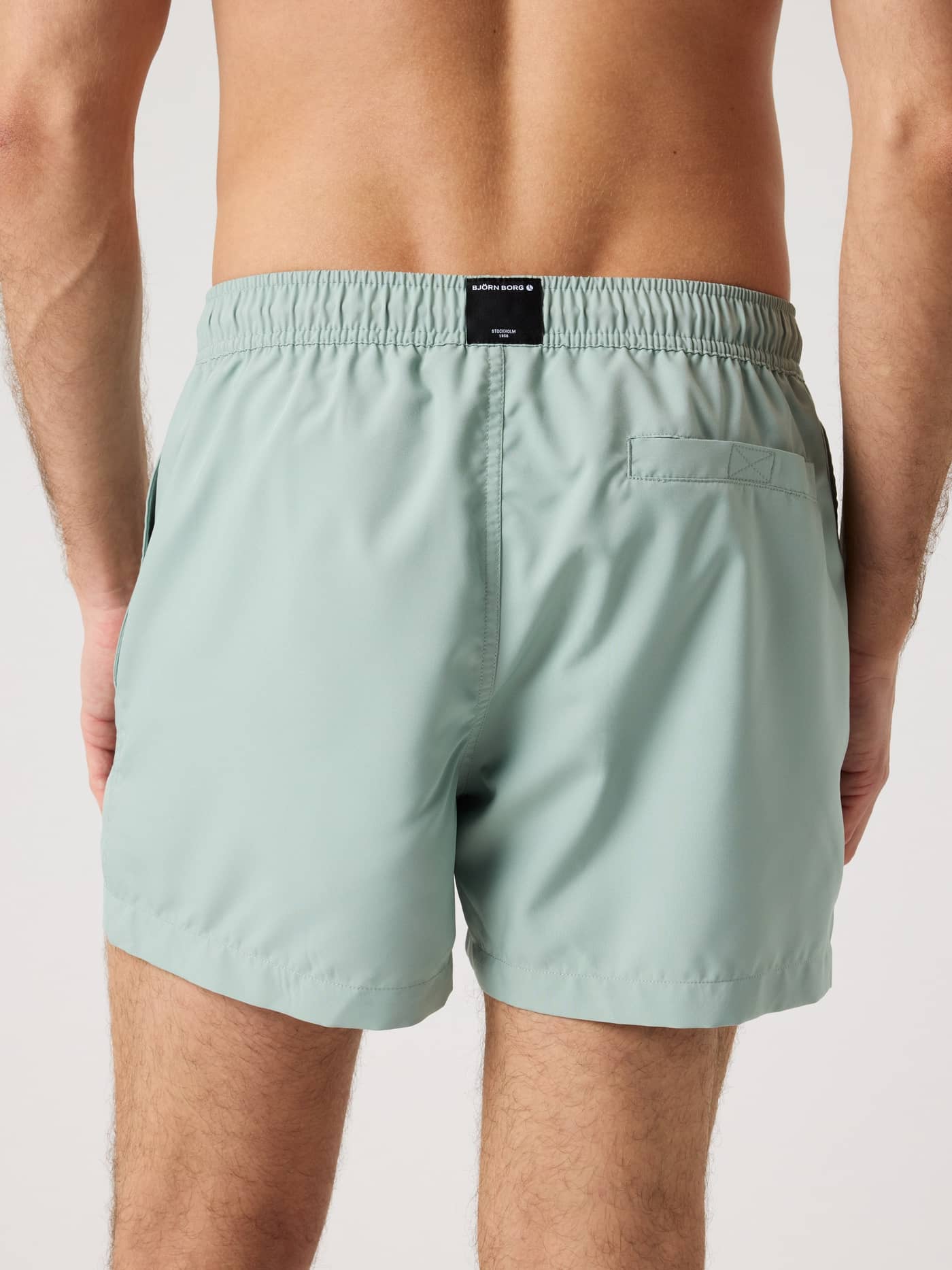 Back view of a man wearing the green Björn Borg Solid Swim Shorts, featuring a functional velcro back pocket and logo label. - Image 2