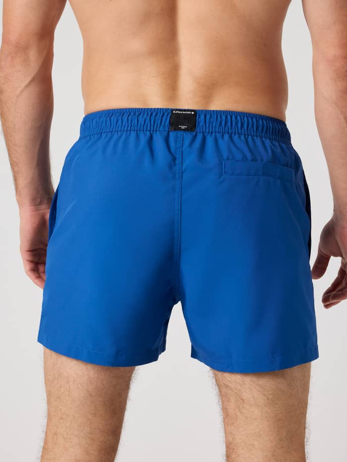 Achteraanzicht van een man in de Borg Solid Swim Shorts in Monaco Blue (Blauw) met een zwart logolabel en achterzak. - Image 2